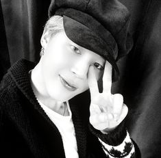 black and white photo of a person wearing a hat making the v sign with their fingers