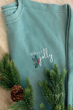 a green sweatshirt with holly embroidered on the chest and pine cones in front of it