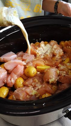 someone pouring milk into a slow cooker filled with meat and potatoes, ready to be cooked