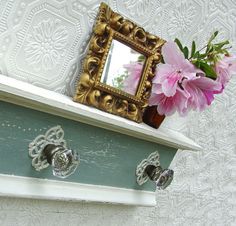 there is a mirror on the shelf with two knobs and a flower in it