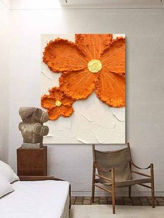 an orange flower is hanging on the wall next to a white bed and two chairs