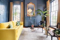 a living room with blue walls, yellow furniture and large mirrors on the windowsill