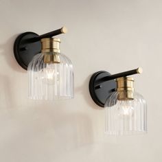 two lights are attached to the wall with clear glass shades and brass fittings on each side