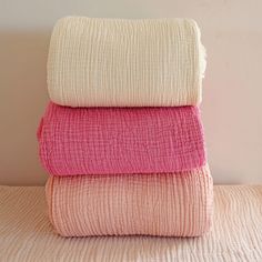 three towels stacked on top of each other in pink, white and beige colors against a wall