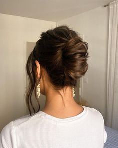 a woman with her hair in a low bun, wearing earrings and a white shirt