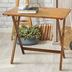 a wooden table with books and plants on it in front of a brick wall next to a ladder