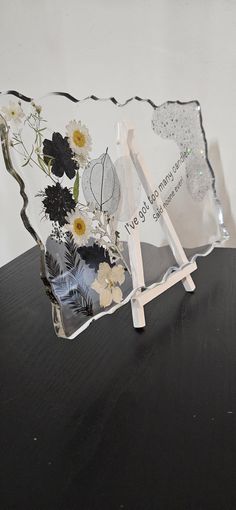 an acrylic sign with flowers on it sitting on top of a wooden table