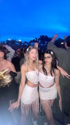 two women dressed in white are posing for the camera at a party with other people