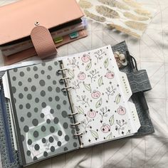 an open planner book sitting on top of a bed next to a purse and wallet