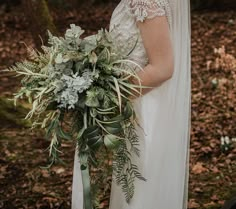 a woman in a wedding dress holding a bridal bouquet with greenery on it