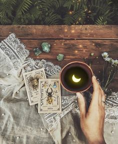 a person holding a cup with a candle in it and playing cards on the table