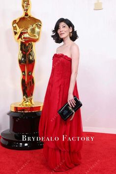 a woman in a red dress standing next to an oscars statue and holding a black purse