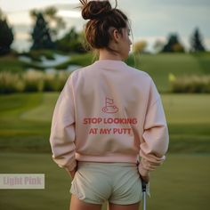 a woman in pink sweatshirt and shorts holding a golf club with the words stop looking at my putt on it