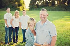 a group of people posing for a photo in the grass with their arms around each other