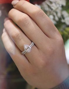 a woman's hand with a diamond ring on top of her finger and flowers in the background