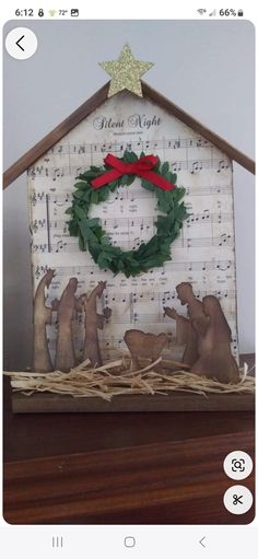 a nativity scene made out of sheet music is displayed on a shelf with a christmas wreath