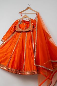 The Persimmon Mirror Lehenga Set features a stunning persimmon orange lehenga adorned with intricate mirror work, paired with a stylish blouse and a matching dupatta. Perfect for festive celebrations, this dazzling ensemble blends traditional charm with modern elegance, making it ideal for weddings, festivals, and special occasions. Orange Chanderi Lehenga With Resham Embroidery, Orange Chanderi Sharara For Reception, Orange Anarkali Set For Reception And Festivals, Orange Sharara With Resham Embroidery For Reception, Orange Chanderi Lehenga With Cutdana, Chanderi Choli In Orange For Receptions, Orange Chanderi Choli For Reception, Orange Dupatta For Reception And Festivals, Orange Sets For Reception And Festivals