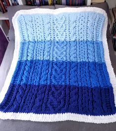 a blue and white knitted blanket sitting on top of a couch next to a book shelf