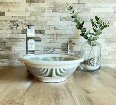 a white bowl sitting on top of a wooden table next to a vase filled with flowers