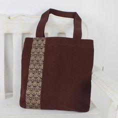 Keawpankanlaya of Thailand creates this pretty tote bag from 100% cotton in a rich mahogany shade. The front of the tote is embellished with traditional Thai yok dok embroidery in cream. The bag closes with a zipper to keep your belongings secure and an open interior pocket keeps small items close at hand. Brown Cotton Bag For Everyday Use, Eco-friendly Brown Canvas Bag For Daily Use, Brown Cotton Shoulder Bag, Brown Cotton Bag For Daily Use, Square Brown Canvas Bag For Daily Use, Eco-friendly Brown Canvas Bag, Brown Square Canvas Bag For Daily Use, Daily Use Brown Cotton Bag, Daily Brown Cotton Bag