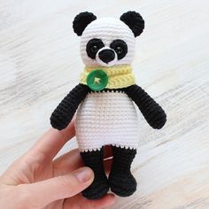 a small crocheted panda bear with a green button on its collar, sitting on a wooden surface