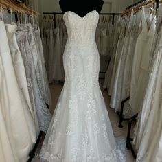 a white wedding dress is on display in a bridal room with other dresses and gowns