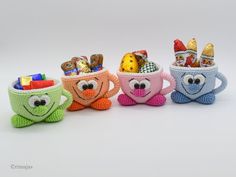 three crocheted mugs filled with candy and candies, each decorated in different colors