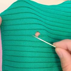 someone is cutting through the side of a green sweater with a pair of scissors and thread