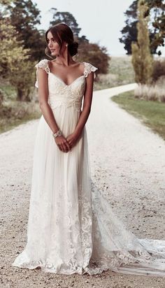 a woman in a wedding dress standing on a dirt road