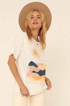 Distressed graphic t-shirt. Vintage-style landscape art print with "Live in the Moment" text. Slashed and distressed detailing at neckline, cuffs, and hem. Round neckline. Short sleeves. Drop shoulder. Relaxed fit. 100% Cotton. Imported top designed and printed in LA. Model wears size S. Cream Graphic Print Top For Summer, Cream Graphic Print Top For Spring, Cream Tops With Screen Print For Spring, Trendy Cream T-shirt For Summer, Spring Cream Top With Screen Print, Cream Tops With Graphic Print And Relaxed Fit, Cream Relaxed Fit Top With Graphic Print, Relaxed Fit Cream Top With Graphic Print, Artsy Printed Summer Tops