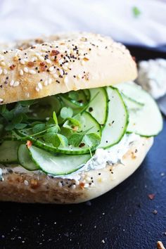 a sandwich with cucumber, lettuce and sesame seeds on it sitting on a black surface