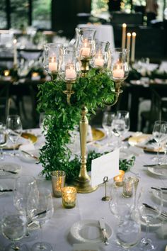 the centerpieces on this table are filled with candles, greenery and wine glasses