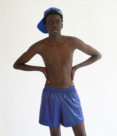 a young man in blue shorts and a hat posing for the camera with his hands on his hips