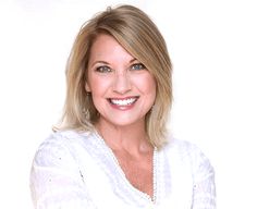 a woman with blonde hair wearing a white shirt and smiling at the camera while standing in front of a white background