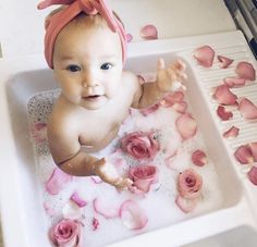 a baby sitting in a bathtub with rose petals on the floor and an interest sign above it