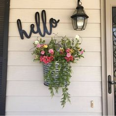 flowers in a basket hanging on the side of a house next to a lamp and door