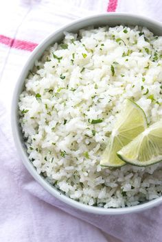 a white bowl filled with rice and limes on top of a table next to a napkin