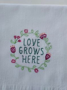 a white towel with embroidered words and flowers around it that says love grows here on the front