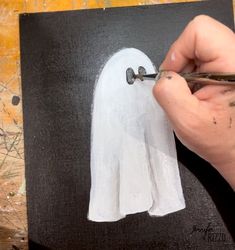 someone is painting a ghost with white paint on a black piece of paper and holding a pair of scissors