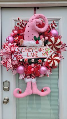 a pink and red christmas wreath with candy cane lane sign on it's front door