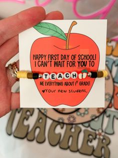 a hand holding a teacher's beaded bracelet with an apple on it and the words happy first day of school i can't wait for you to teach