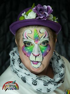 a woman with face paint and flowers on her head wearing a purple hat, scarves and scarf