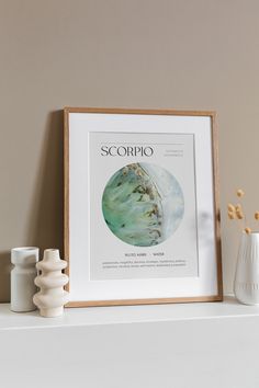 a white vase sitting on top of a shelf next to a framed poster with the word scorpioo