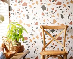 a wooden chair sitting next to a potted plant on top of a table in front of a wall