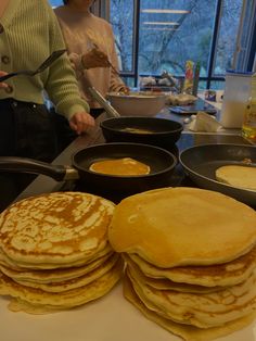 pancakes are stacked on top of each other in front of a woman preparing pancakes