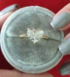 a woman's hand holding a ring with a heart shaped diamond on it,