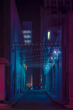 an alley way with lights strung from the ceiling and buildings in the background at night