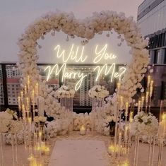 a wedding arch with flowers and candles in the shape of a heart that says will you marry me?