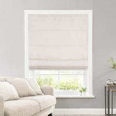 a living room with a white couch and window covered in roman blind shades on the windowsill