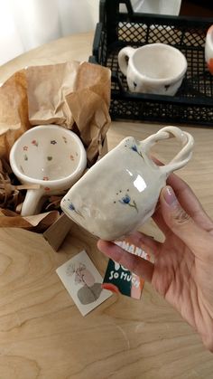 a person holding up a small cup on top of a wooden table next to other items